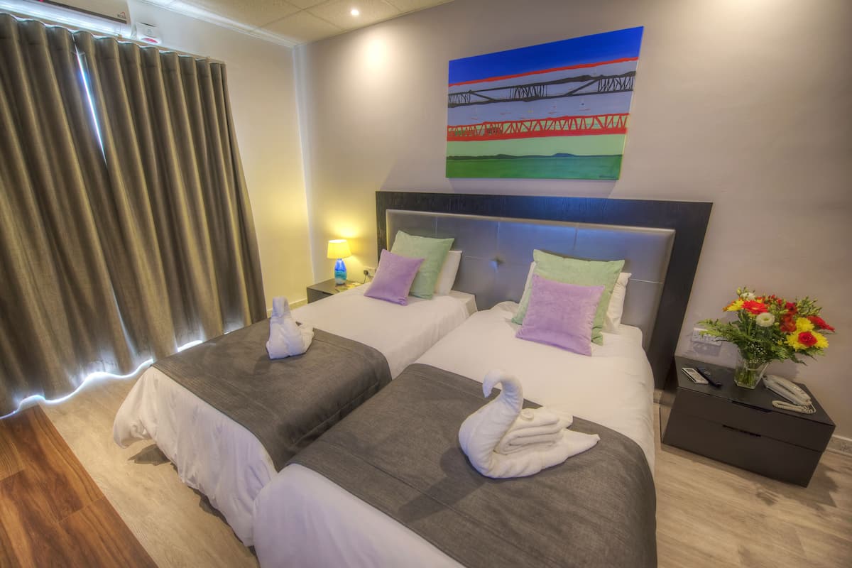 A hotel room with two beds, a nightstand with a phone, and a painting on the wall.