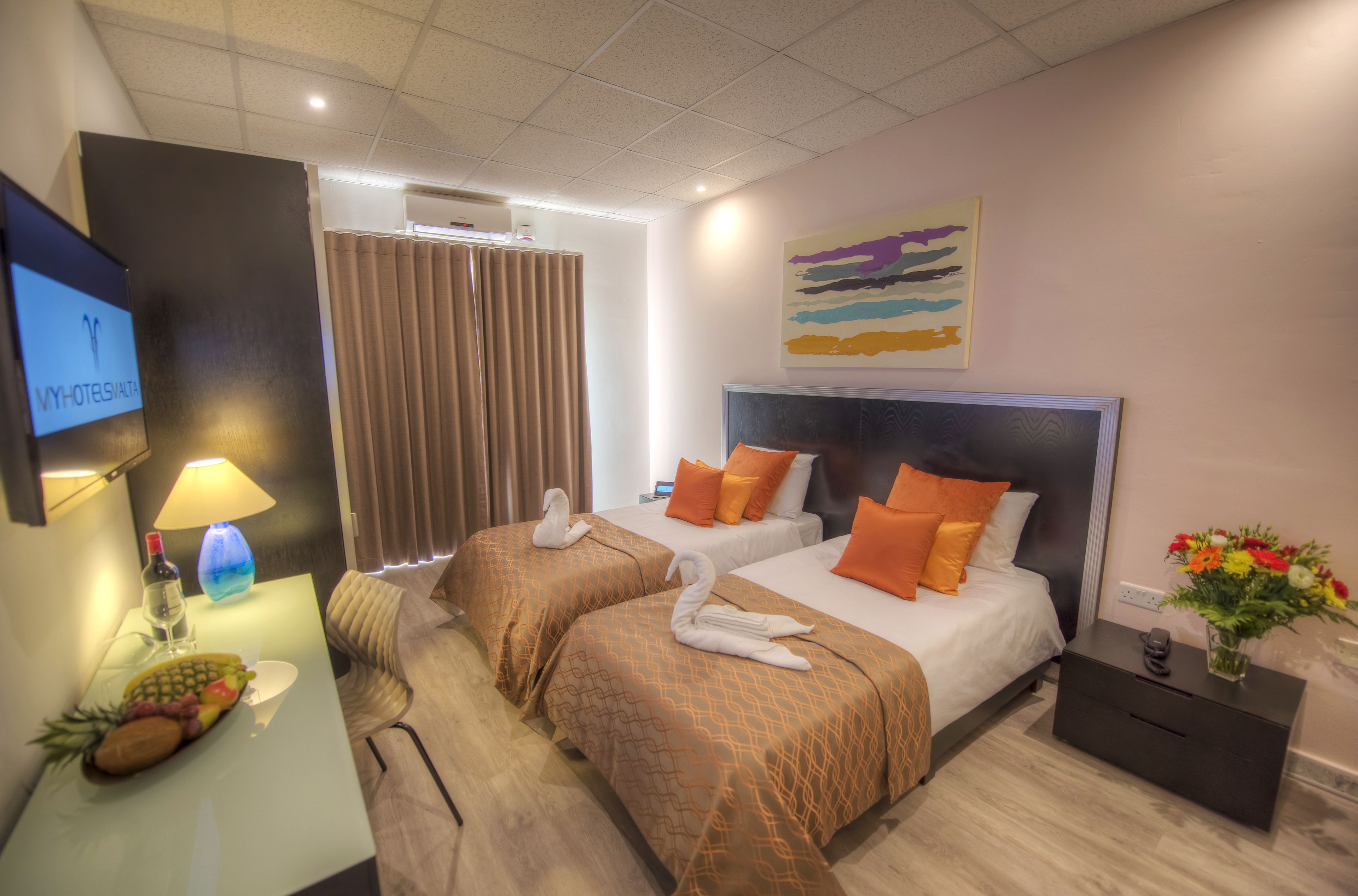 Une chambre d’hôtel avec deux lits, une télévision, un bureau avec une lampe et un tableau au mur.