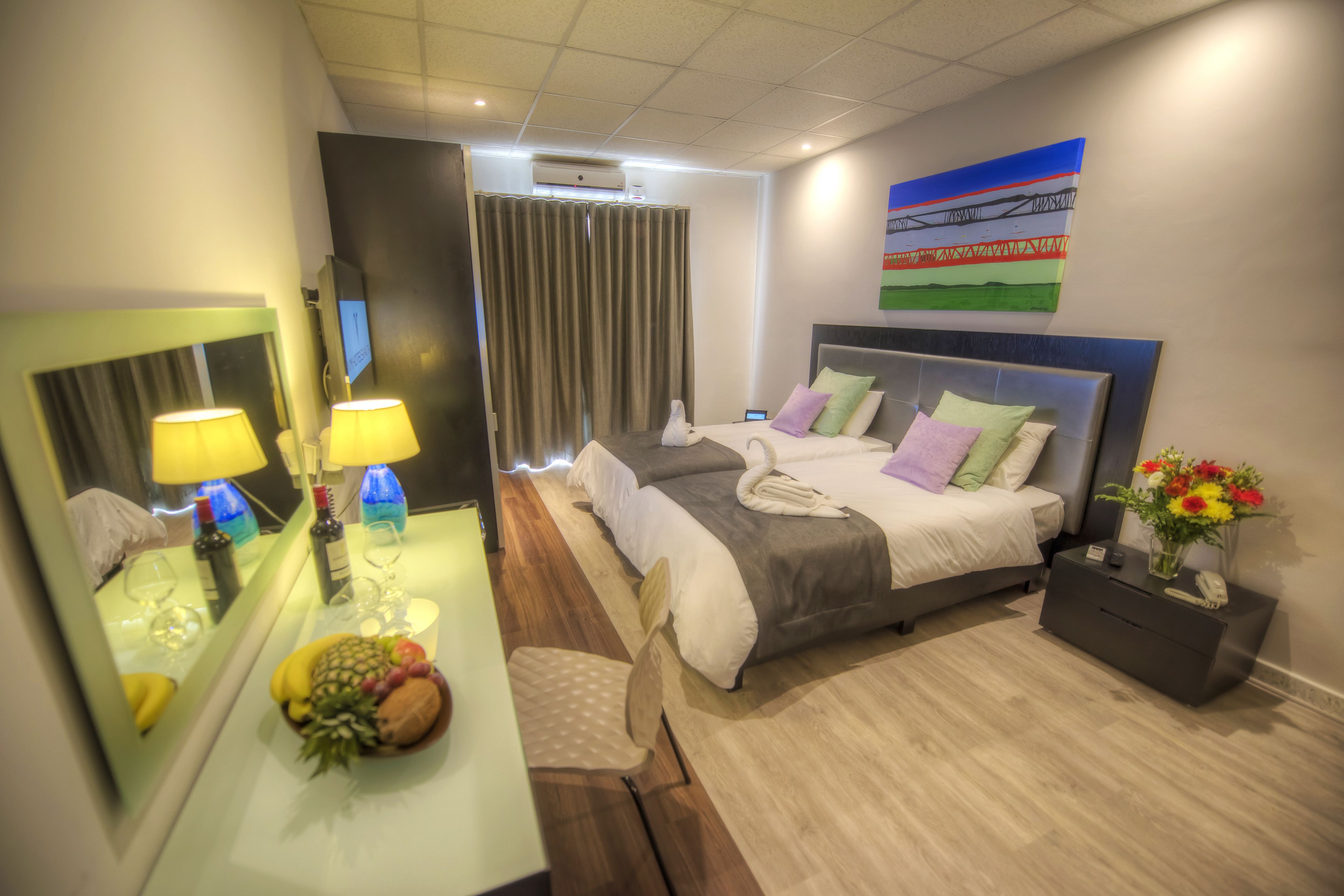 A modern hotel room with a large bed, bedside tables, a mirror, and a fruit bowl.