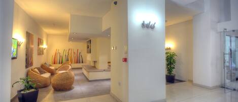 A modern lobby with a reception desk, seating area with wicker chairs, and potted plants.