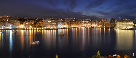 A waterfront cityscape at night with illuminated buildings and boats on the water.