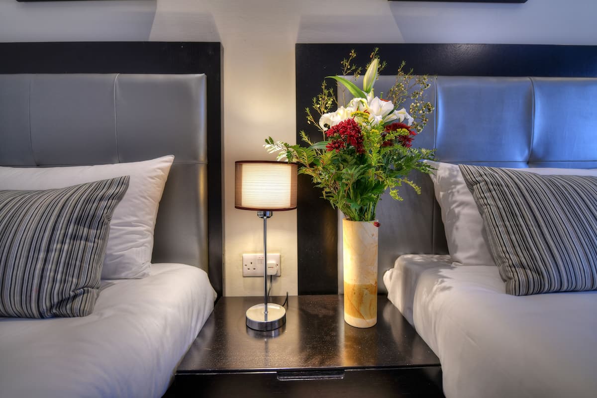 A hotel room with two beds, a nightstand with a lamp, and a vase with flowers.