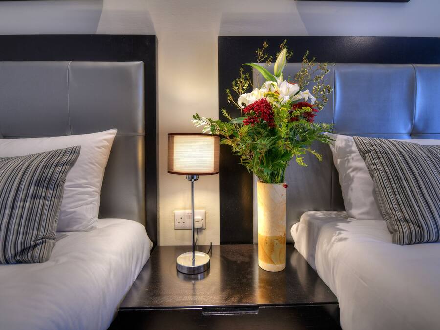 A hotel room with two beds, a nightstand with a lamp, and a vase with flowers.