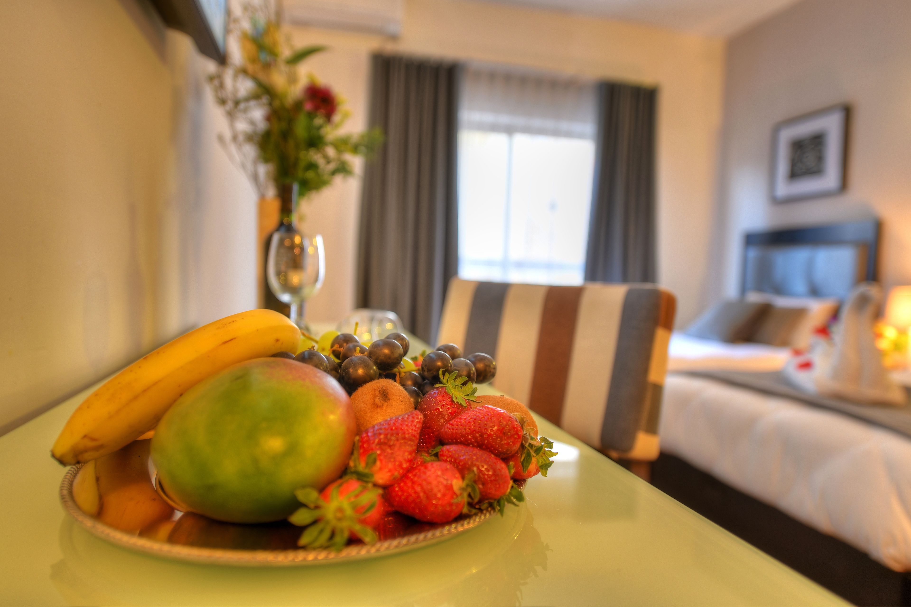 Una bandeja de frutas sobre una mesa, con una cama y cortinas al fondo.