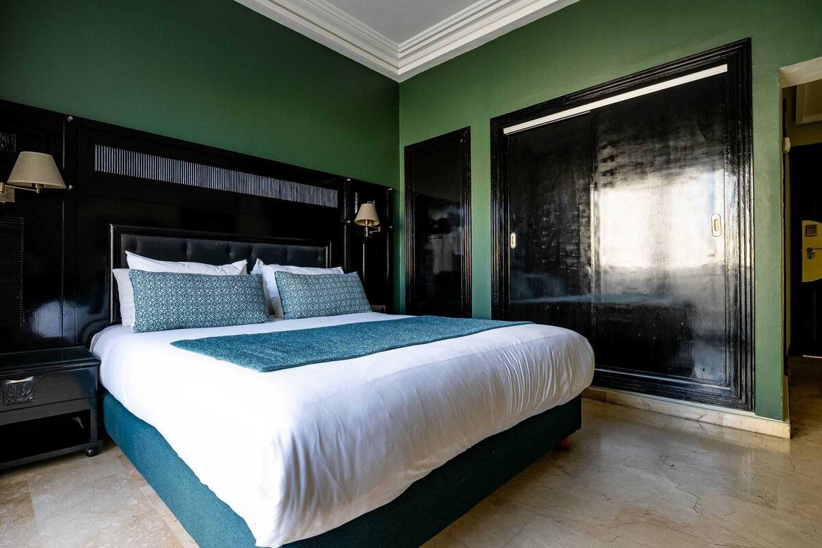 Un grand lit avec une tête de lit sombre, une literie blanche et des touches de couleur turquoise.