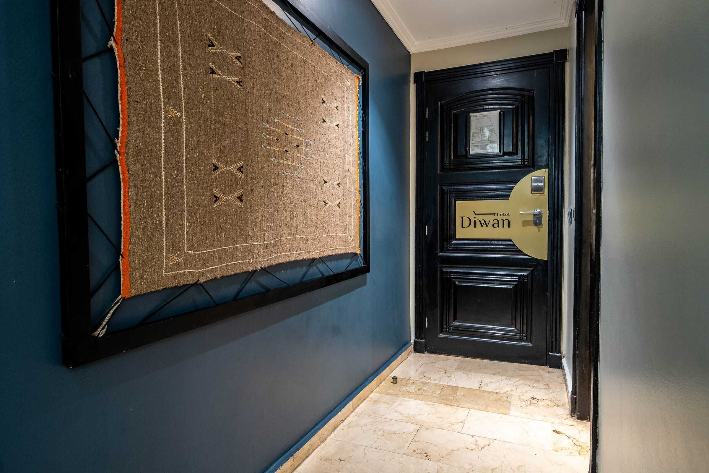 Een gang met een donkerblauwe muur, een lijstwerk en een deur met de tekst 'Diwan Hotel'.