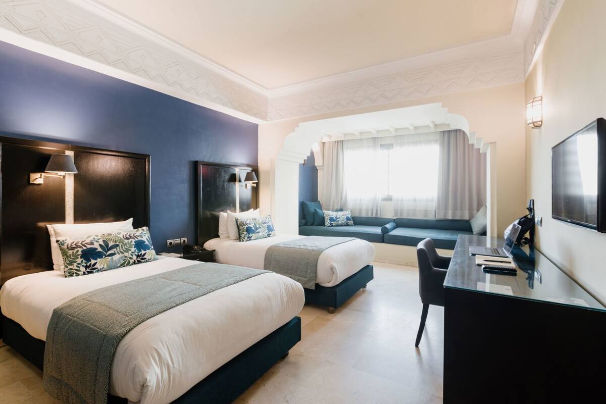 Une chambre d’hôtel avec deux lits, un bureau, une chaise, une télévision et une fenêtre avec des rideaux.