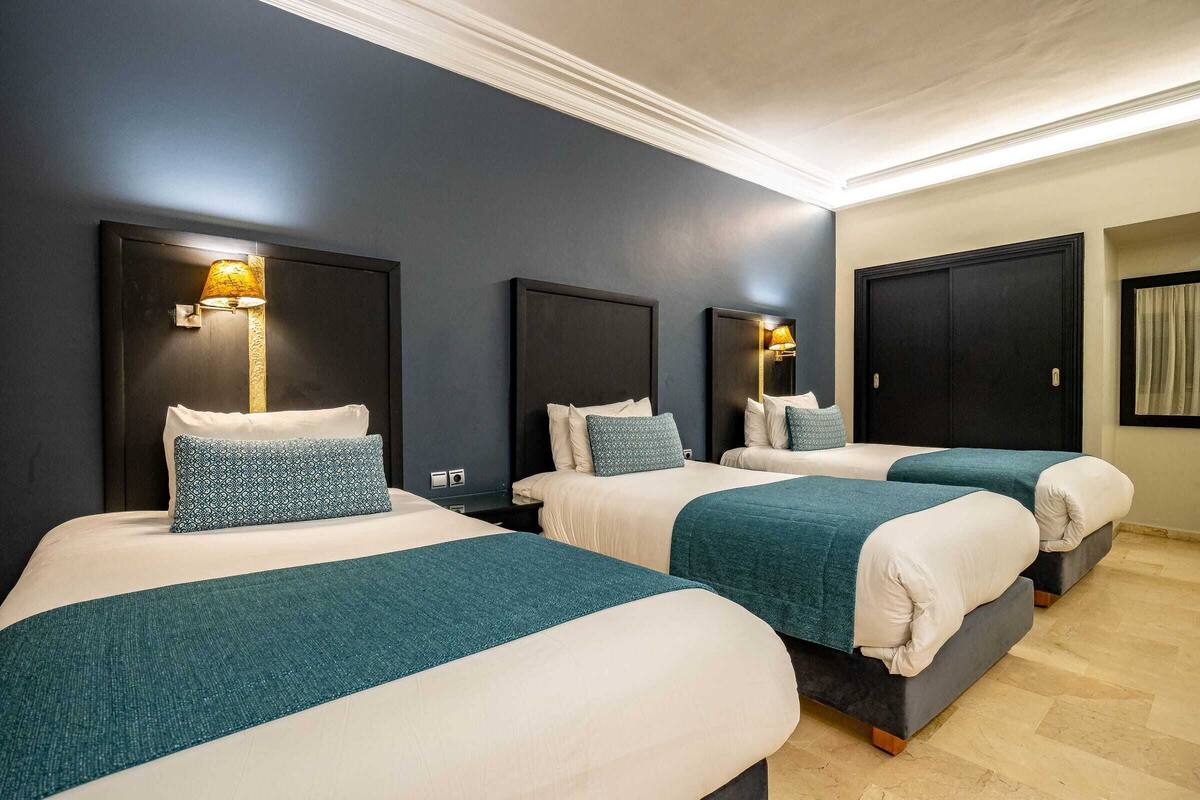 Une chambre d’hôtel avec trois lits, chacun doté d’une tête de lit et de lampes de chevet.