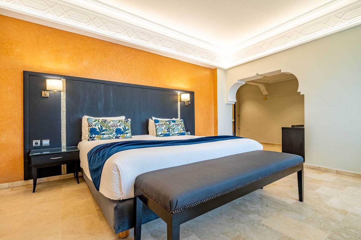 Une chambre moderne avec un grand lit, deux tables de chevet, un banc et un plafond décoratif.