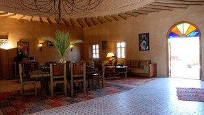 A spacious lobby with a high ceiling, a central dining area with chairs and a table, and a large arched doorway leading outside.