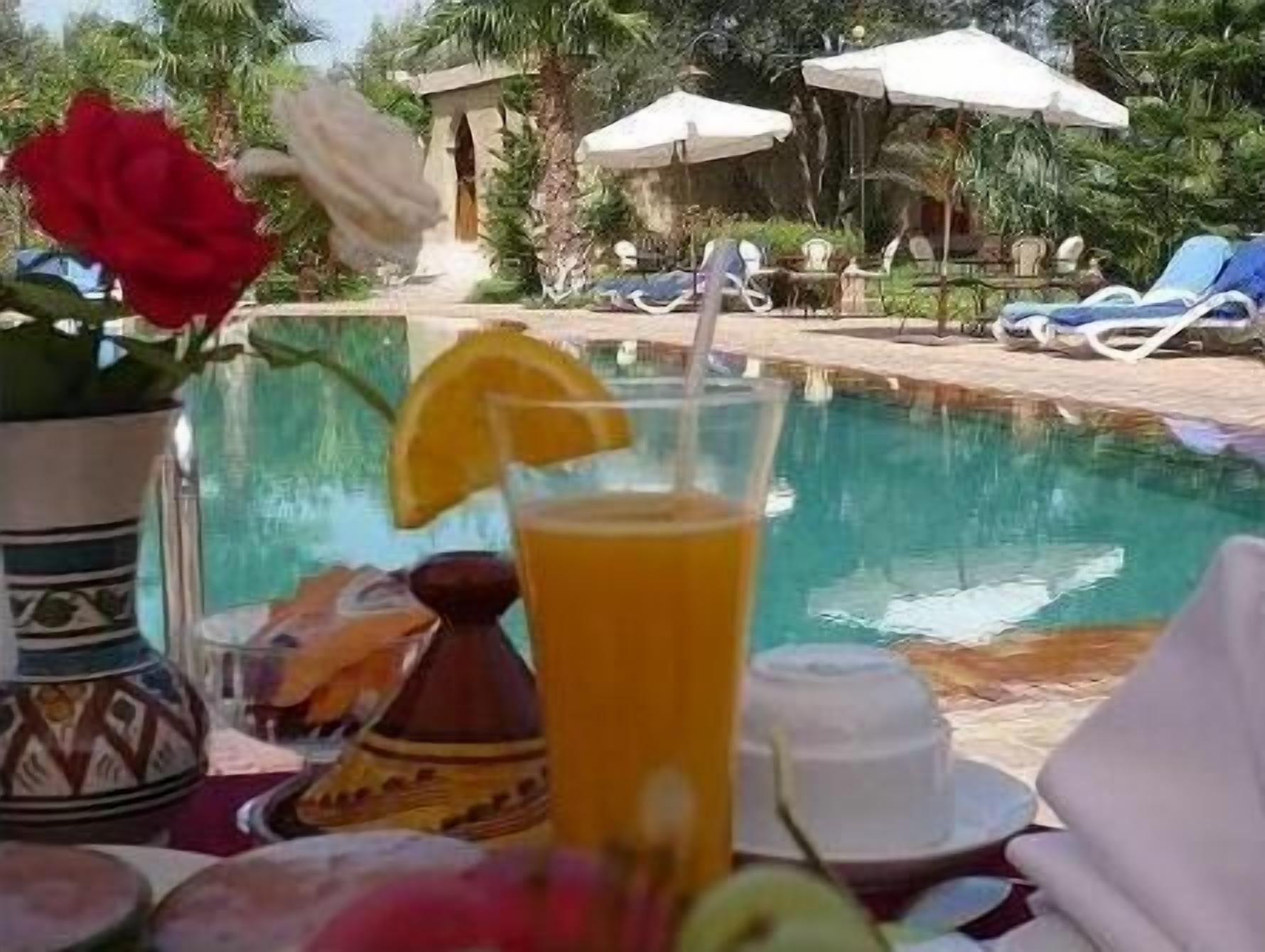 Un tavolo vicino alla piscina con una bevanda, un vaso con un fiore rosso e una bottiglia decorativa.