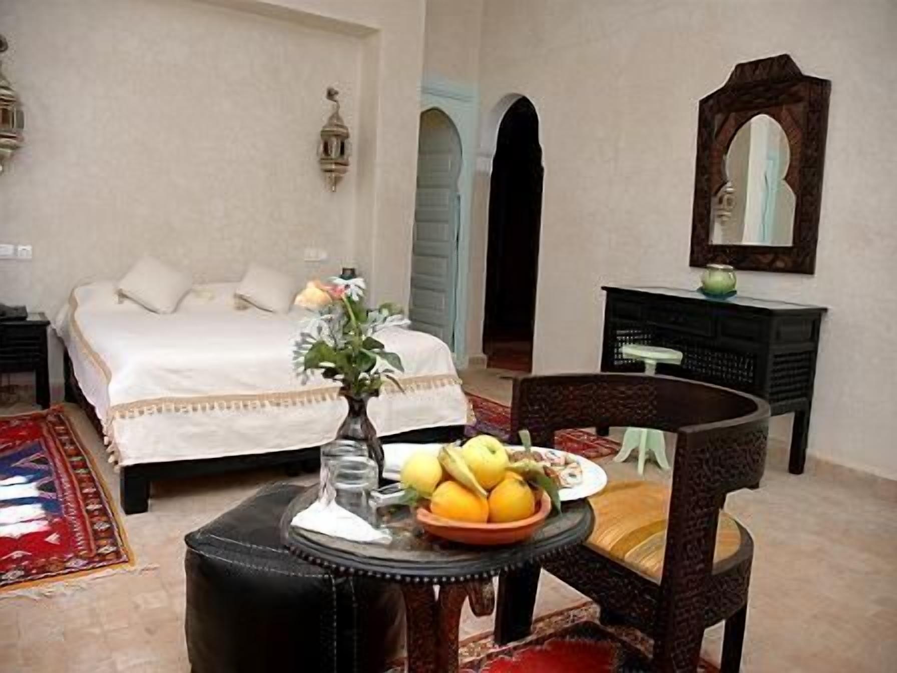 A bedroom with a bed, a dresser, a chair, and a table with fruit.
