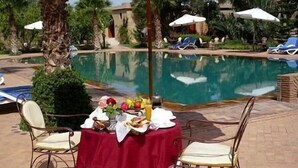 A poolside dining area with a table set for two, surrounded by palm trees and lounge chairs.