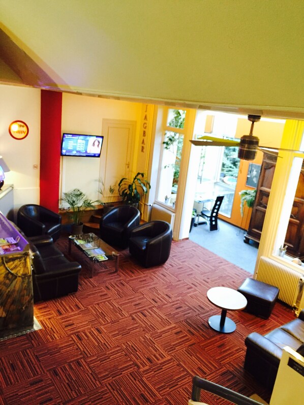 A hotel lobby with a red carpet, black leather sofas, a small table, and a television on the wall.