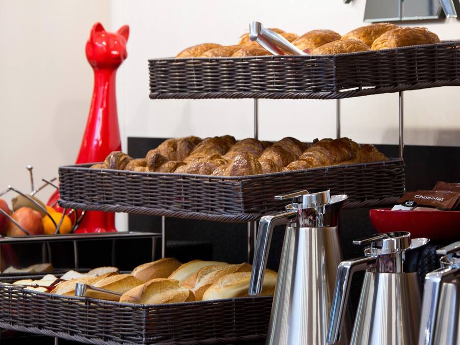 A breakfast buffet with bread, pastries, and a red cat-shaped vase.