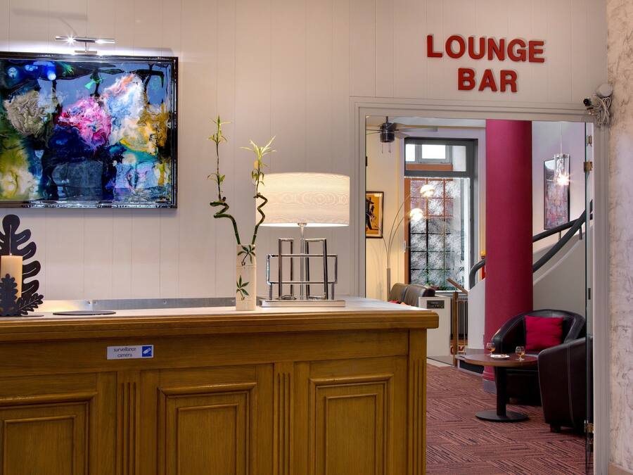 Espaço de bar lounge com balcão de recepção de madeira, uma pintura abstrata colorida e uma placa indicando o bar lounge.