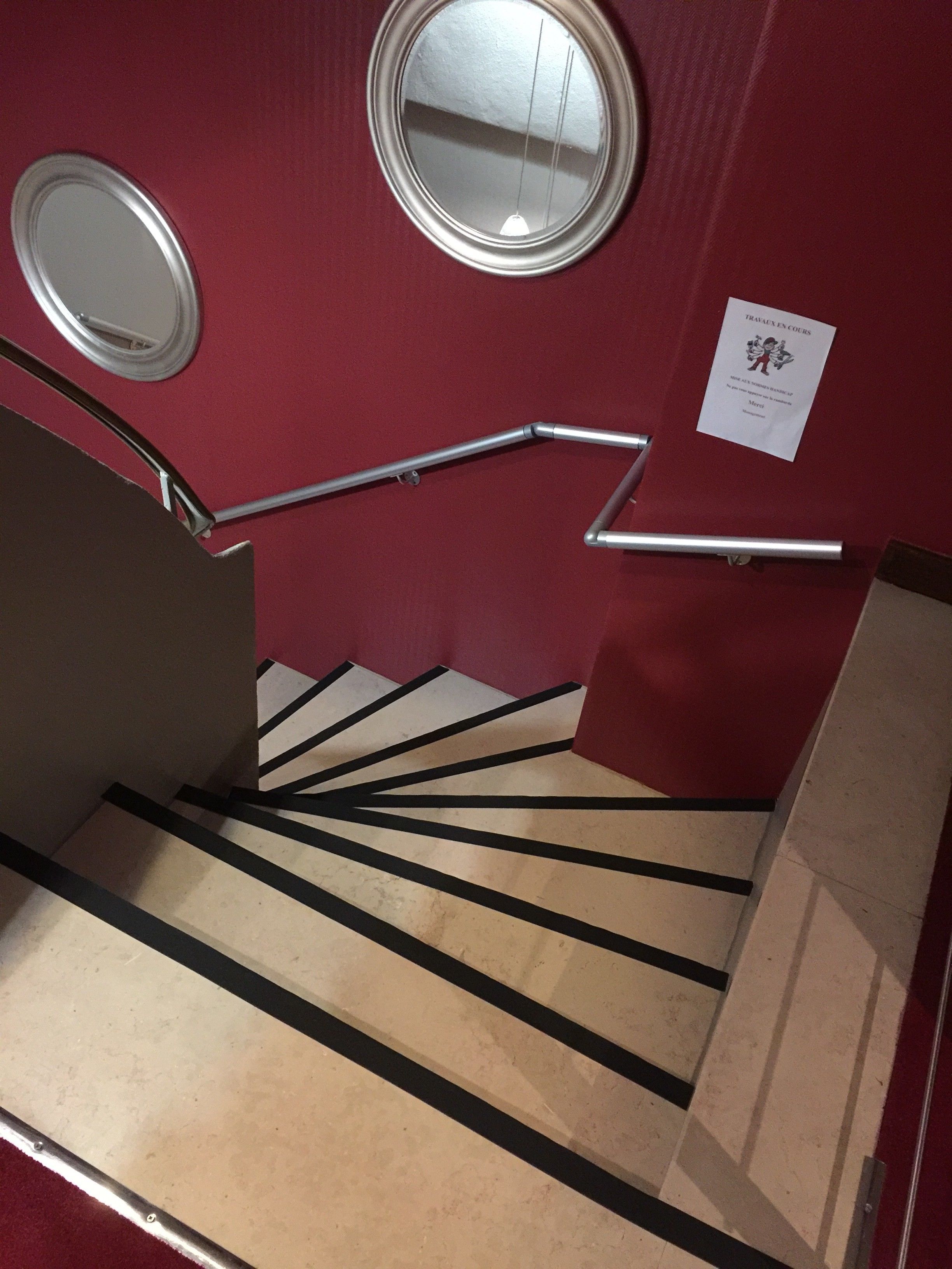 Eine Treppe mit Geländern, einer roten Wand und zwei runden Spiegeln.