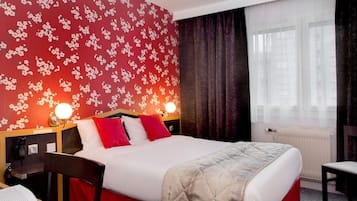A hotel room with a large bed, two bedside tables, a chair, a desk, a lamp, and a window with curtains.