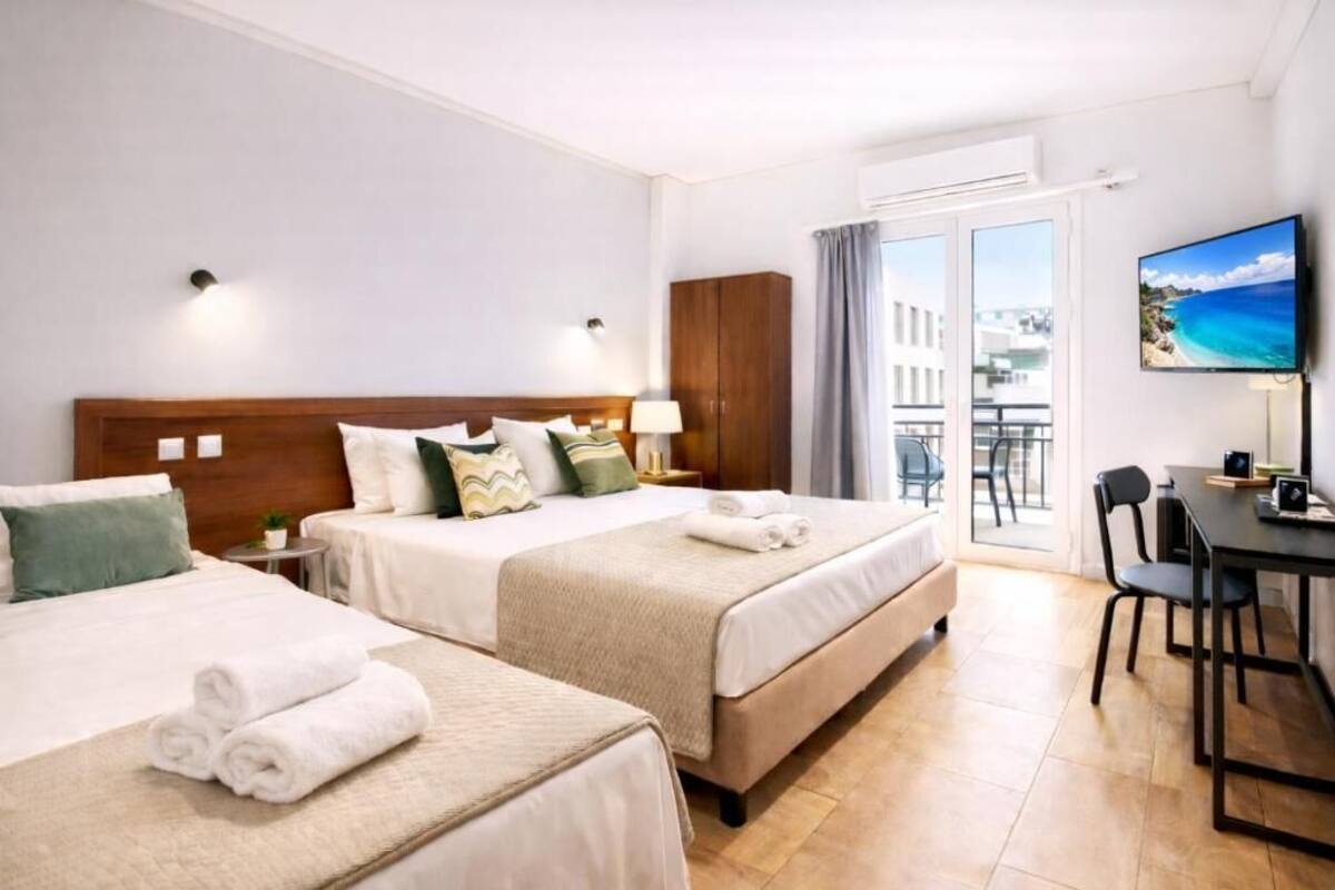 A hotel room with two beds, a balcony, a TV, and a dining area.
