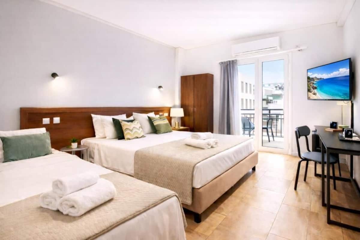 A hotel room with two beds, a balcony, a TV, and a dining area.