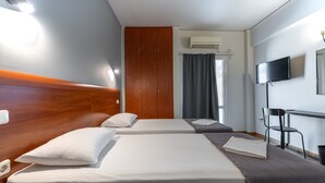 Habitación de hotel con dos camas, cabecera de madera, televisor de pantalla plana, equipo de aire acondicionado y escritorio con silla.