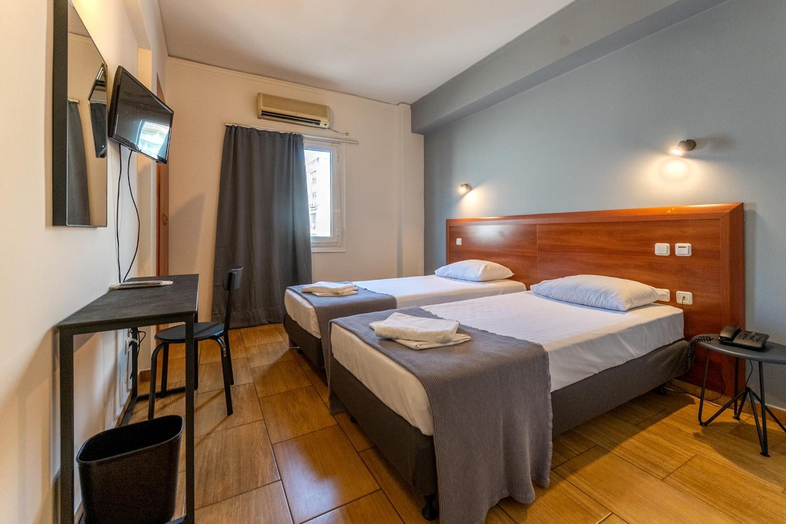 A hotel room with two beds, a desk, a chair, a TV mounted on the wall, and a small table with a phone.