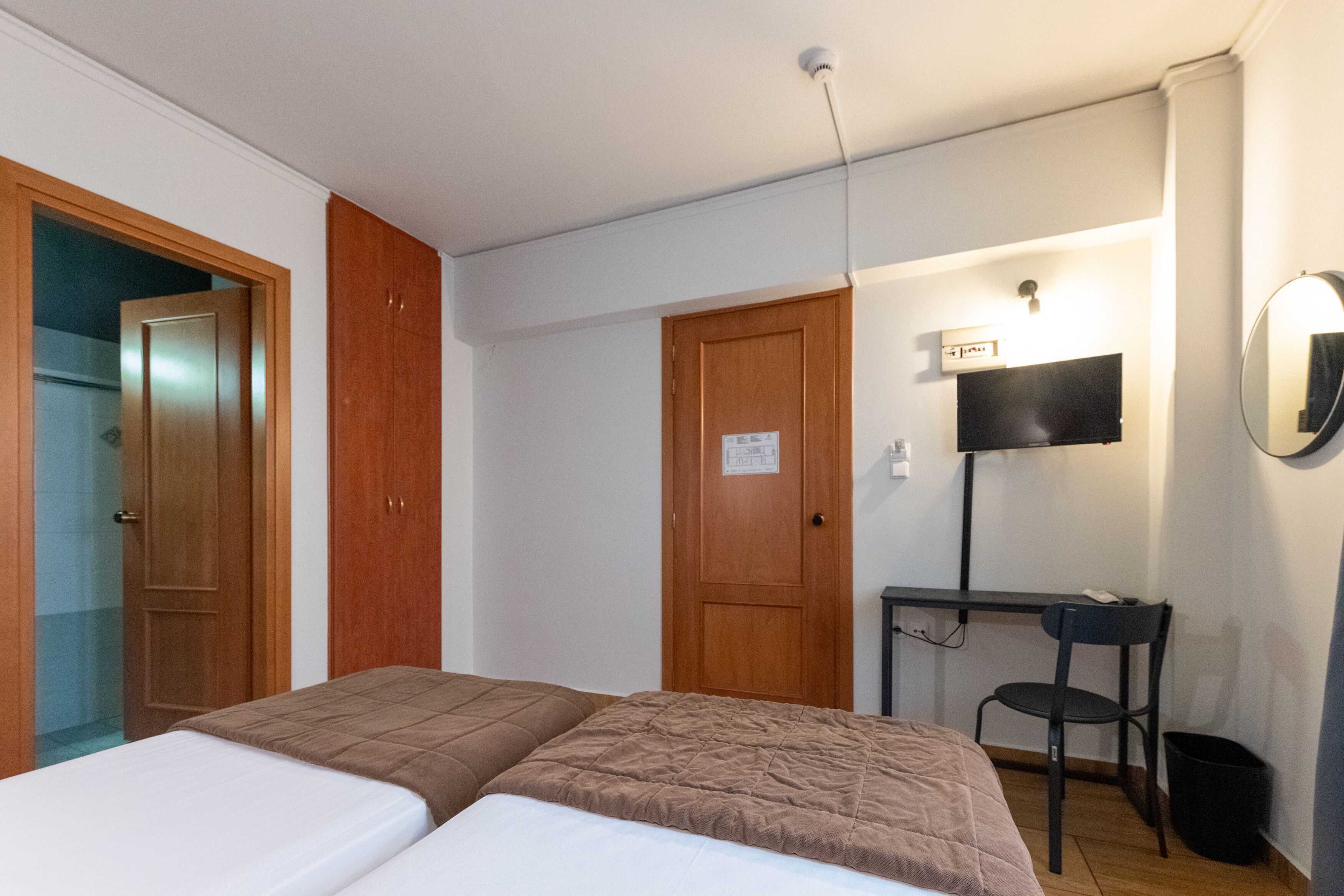 A room with two beds, a desk, a chair, a TV, and a door.