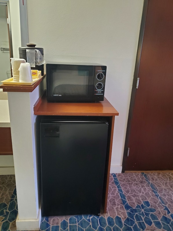 Una kitchenette compacta con microondas y refrigerador sobre una encimera de madera, una bandeja con tazas y una cafetera, y un piso con diseño.