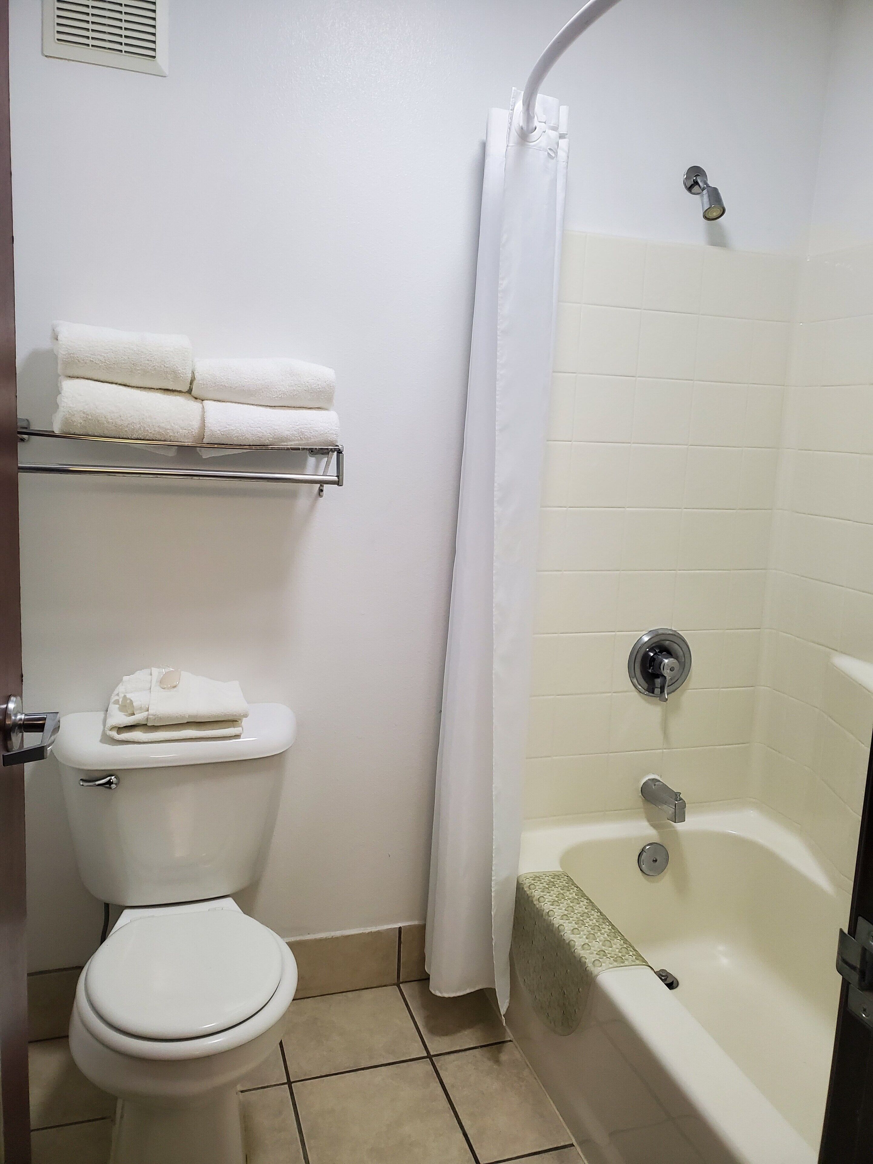 A bathroom with a toilet, a shower with a curtain, and a shelf with towels.