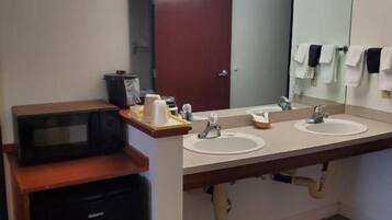 A bathroom with two sinks, a mirror, a microwave, and a trash bin.