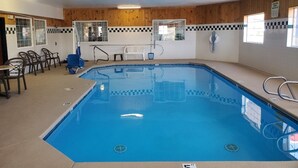 A swimming pool with a tiled deck, a lounge area with chairs, and a wooden wall with a checkered pattern.