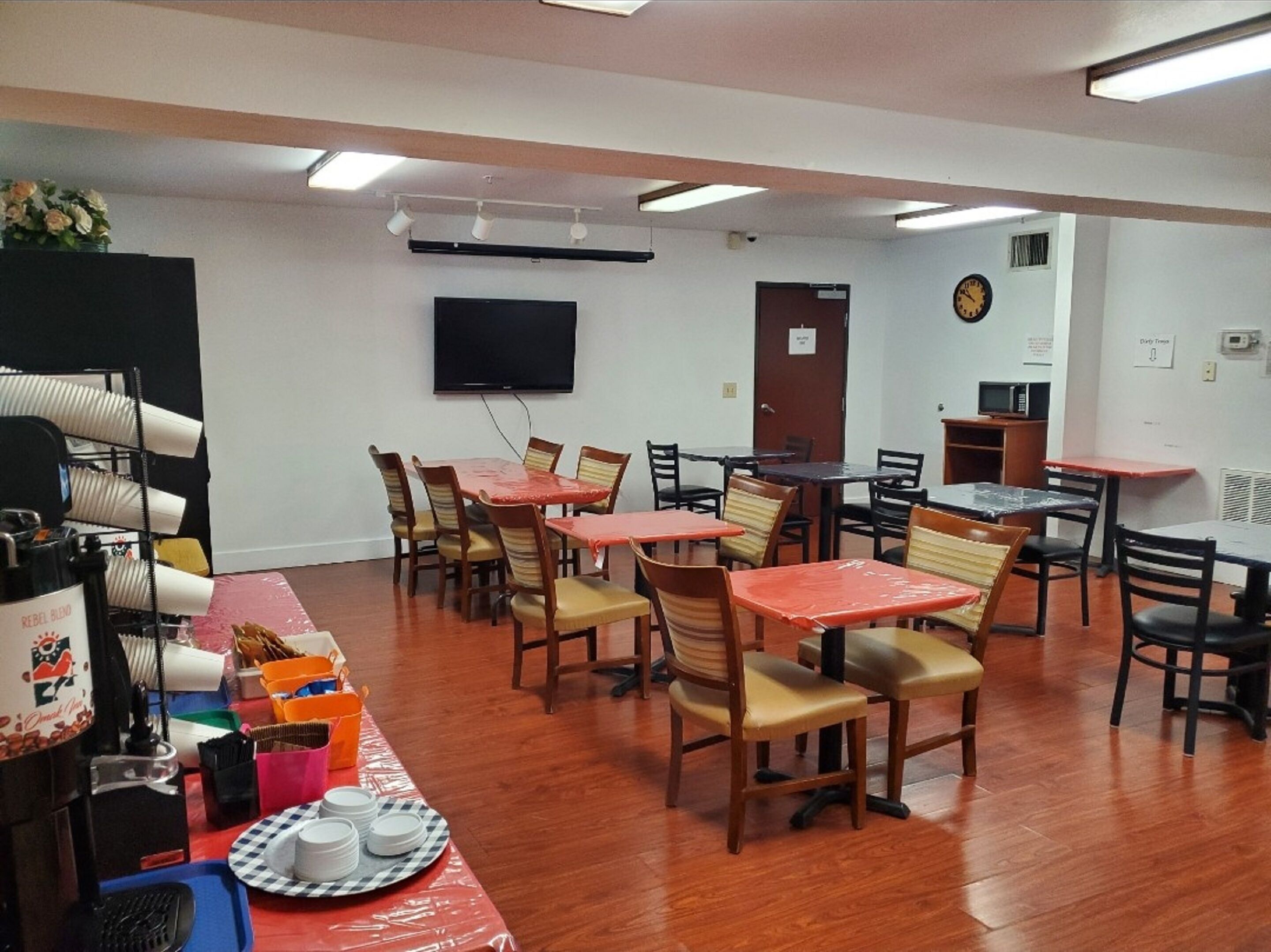 A conference room with multiple tables and chairs, a flat-screen TV mounted on the wall, and a clock on the wall.
