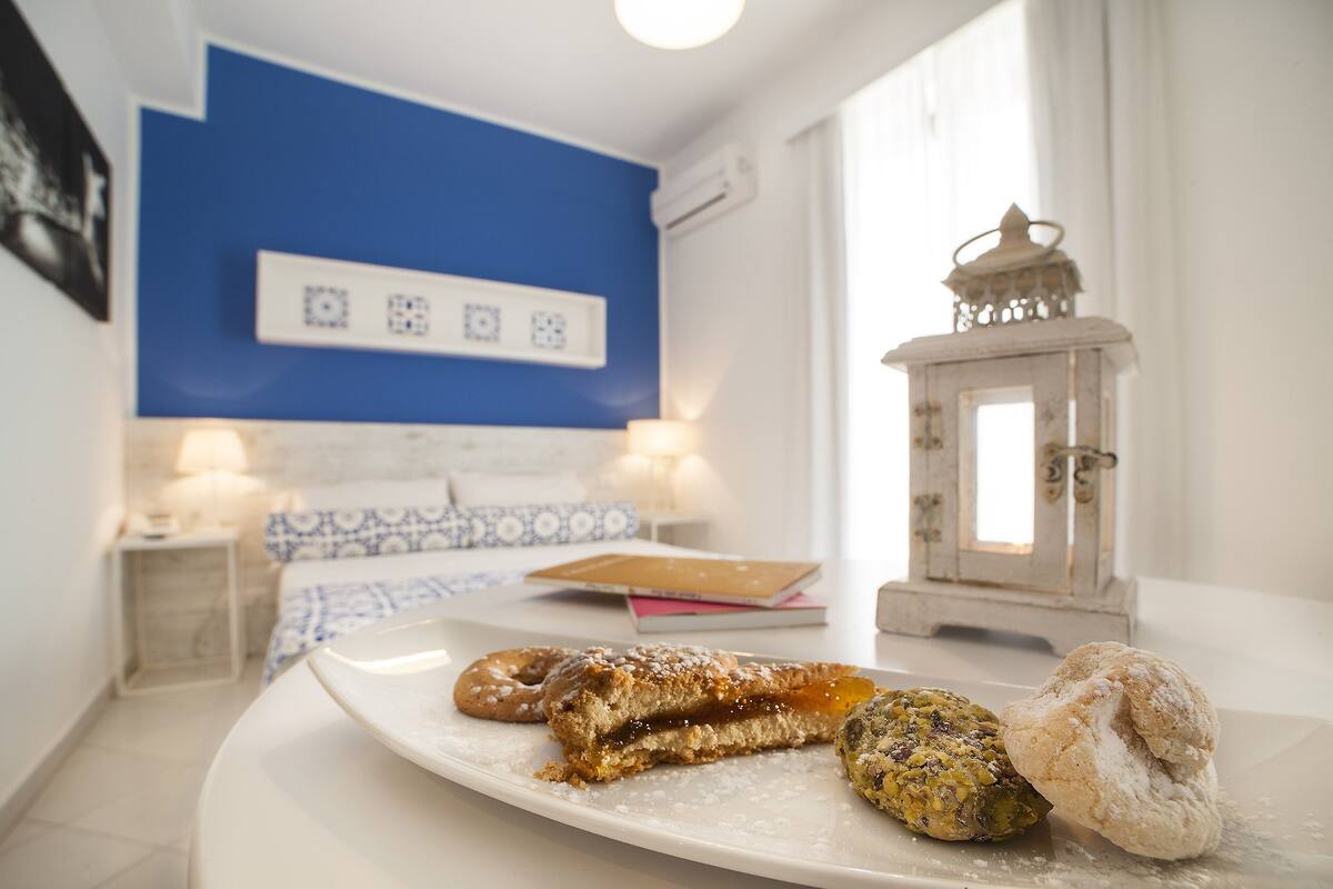 A room with a bed, bedside table, and a plate with pastries.