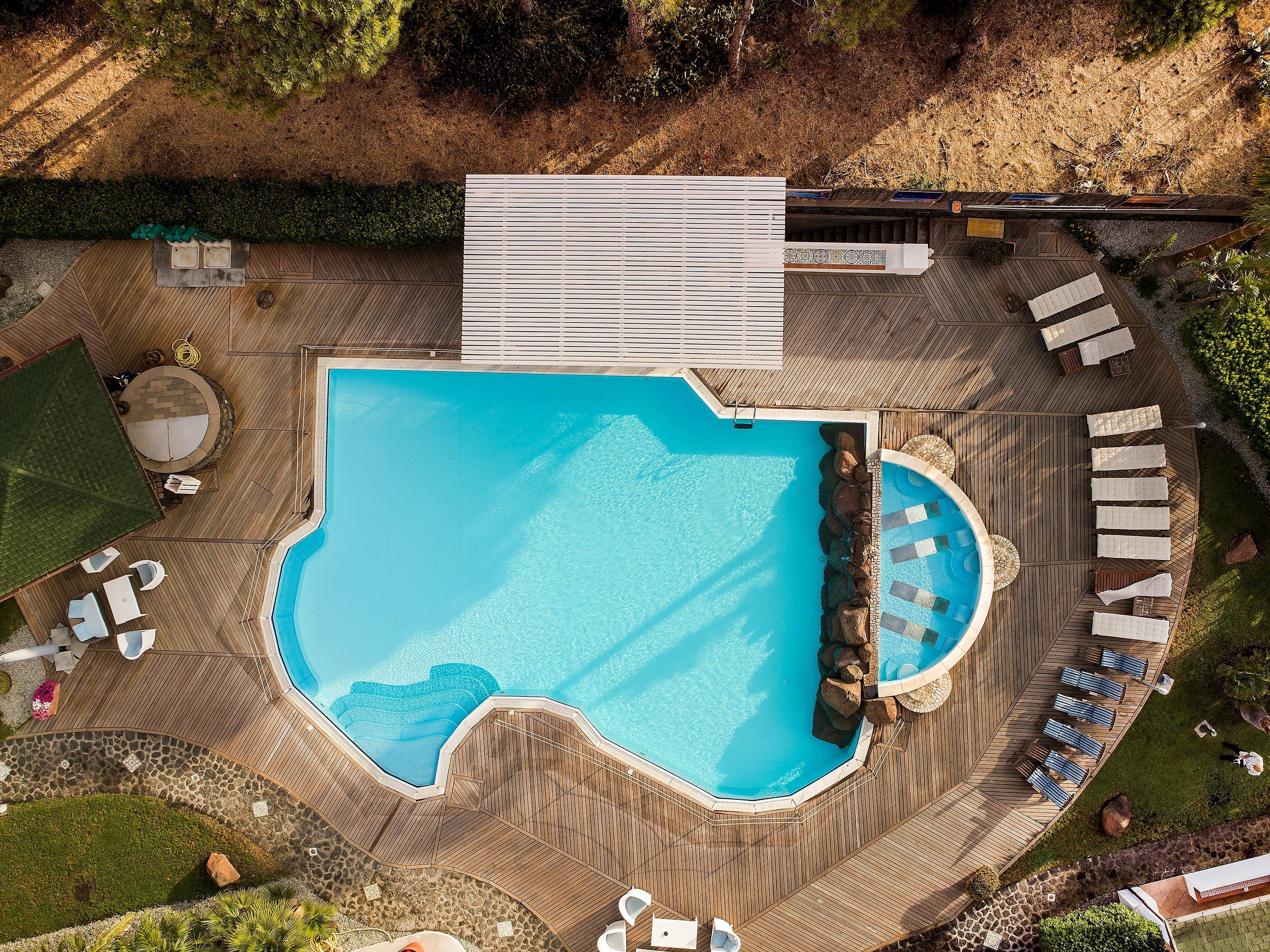 Vista aérea de un resort con una amplia piscina, terraza de madera y zona de estar con tumbonas.