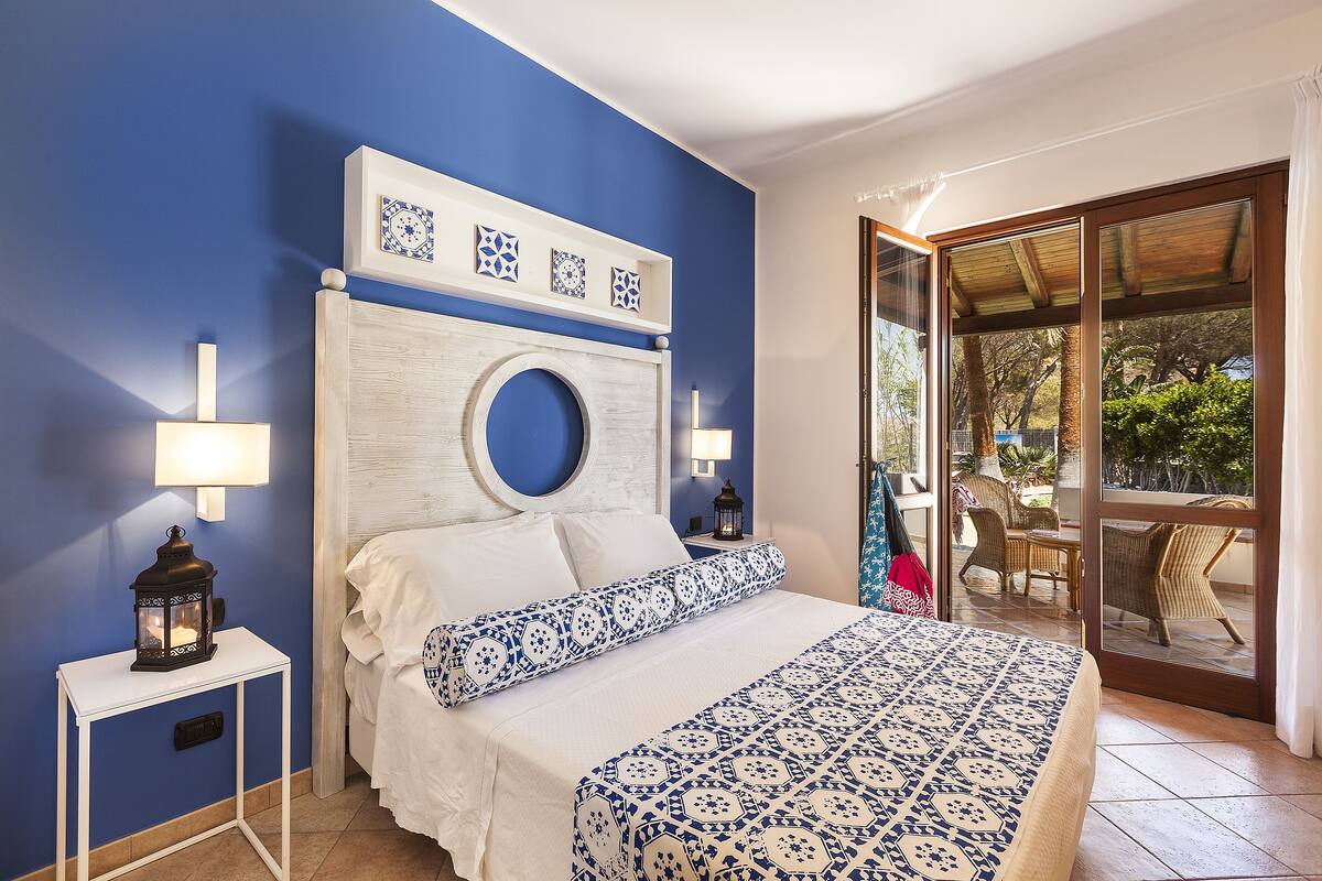 A bedroom with a blue wall, a white headboard with a circular design, a bed with white and blue bedding, and a nightstand with a lantern.