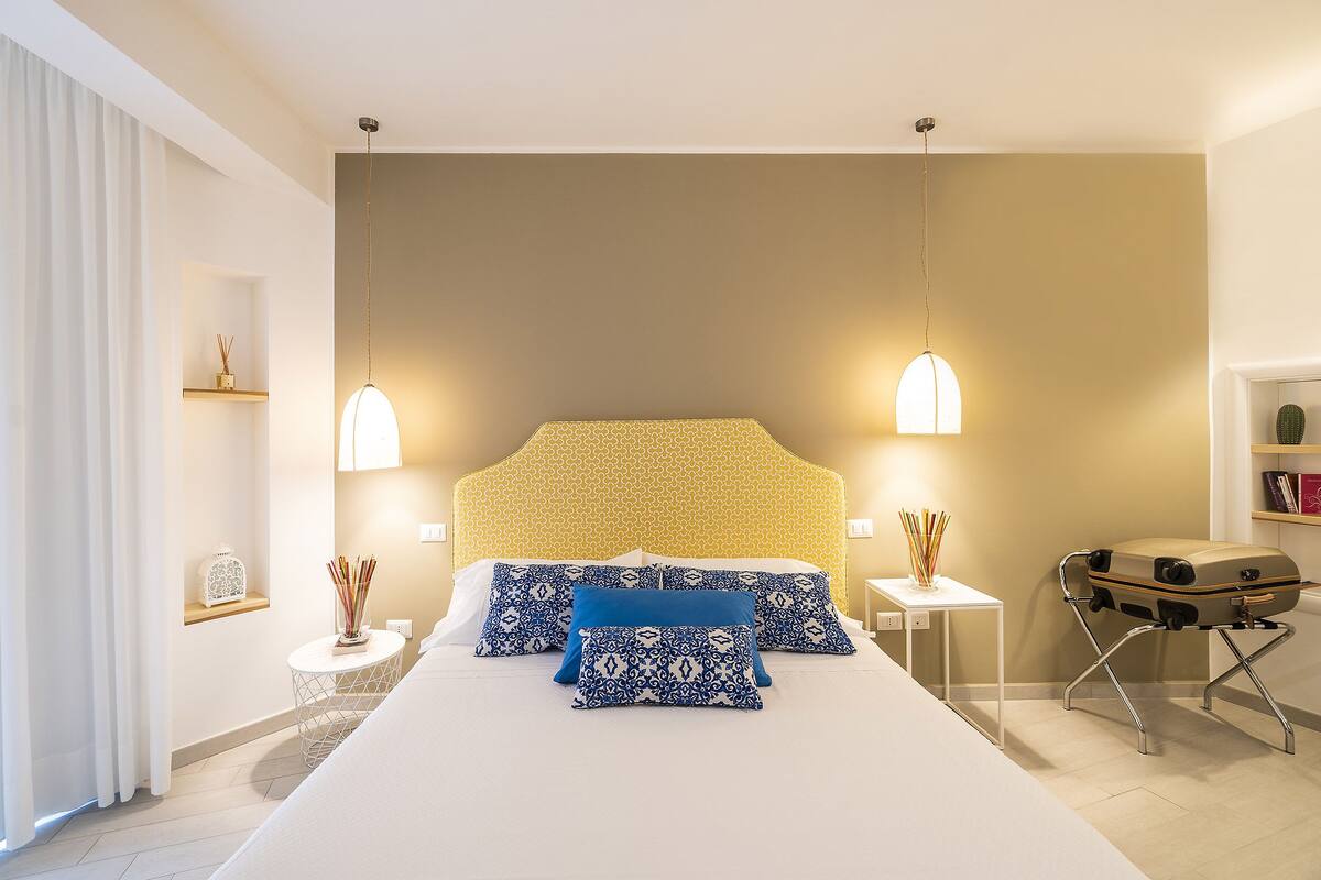 A neatly arranged bedroom with a large bed, bedside lamps, a small table, and a portable grill.