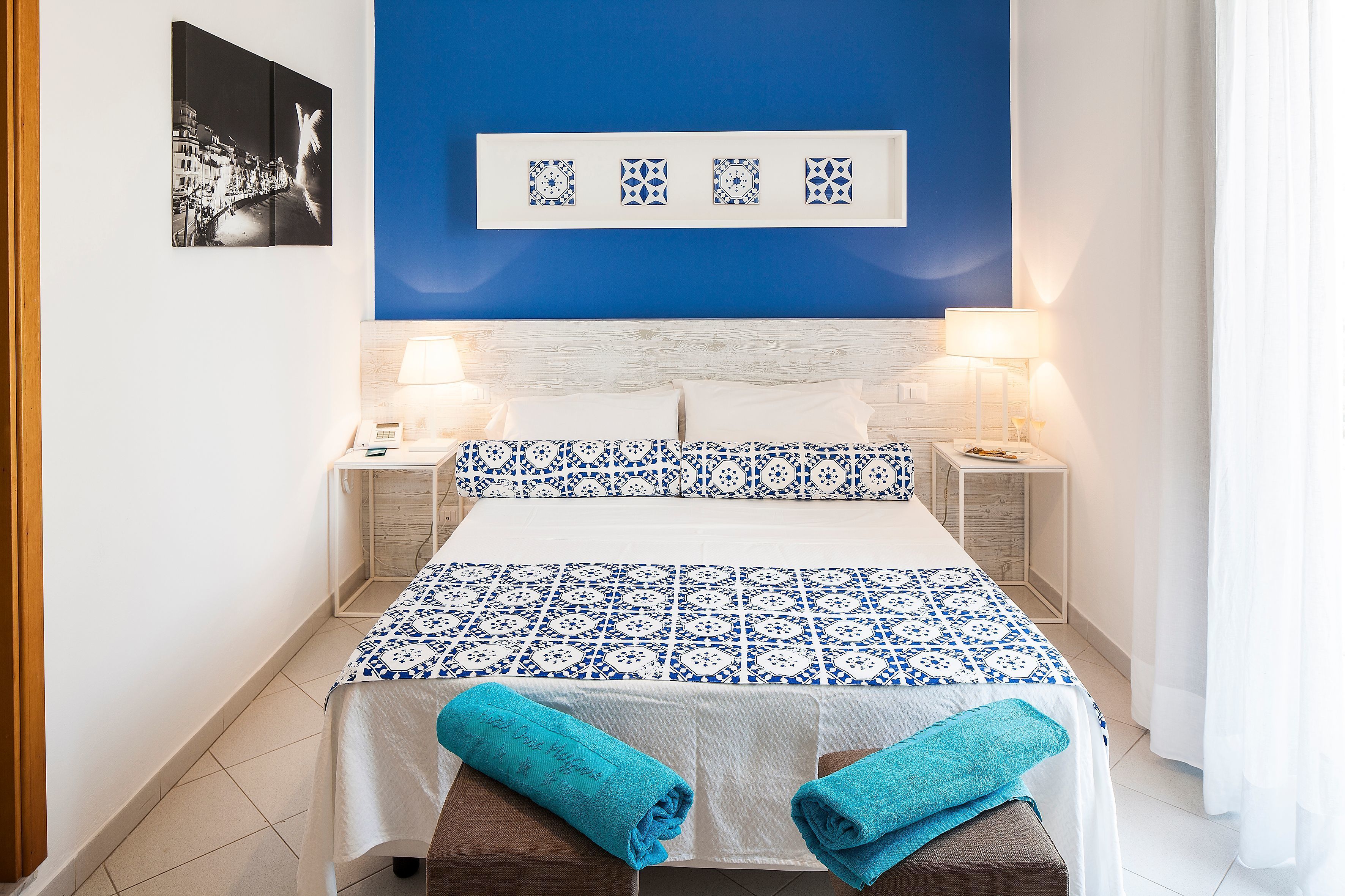 Habitación de hotel ordenada con cama, mesitas de noche y una pared azul de acento.