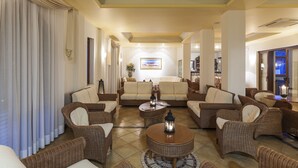 Amplia sala de estar con mobiliario de mimbre, una mesa de centro y un ventanal con cortinas.
