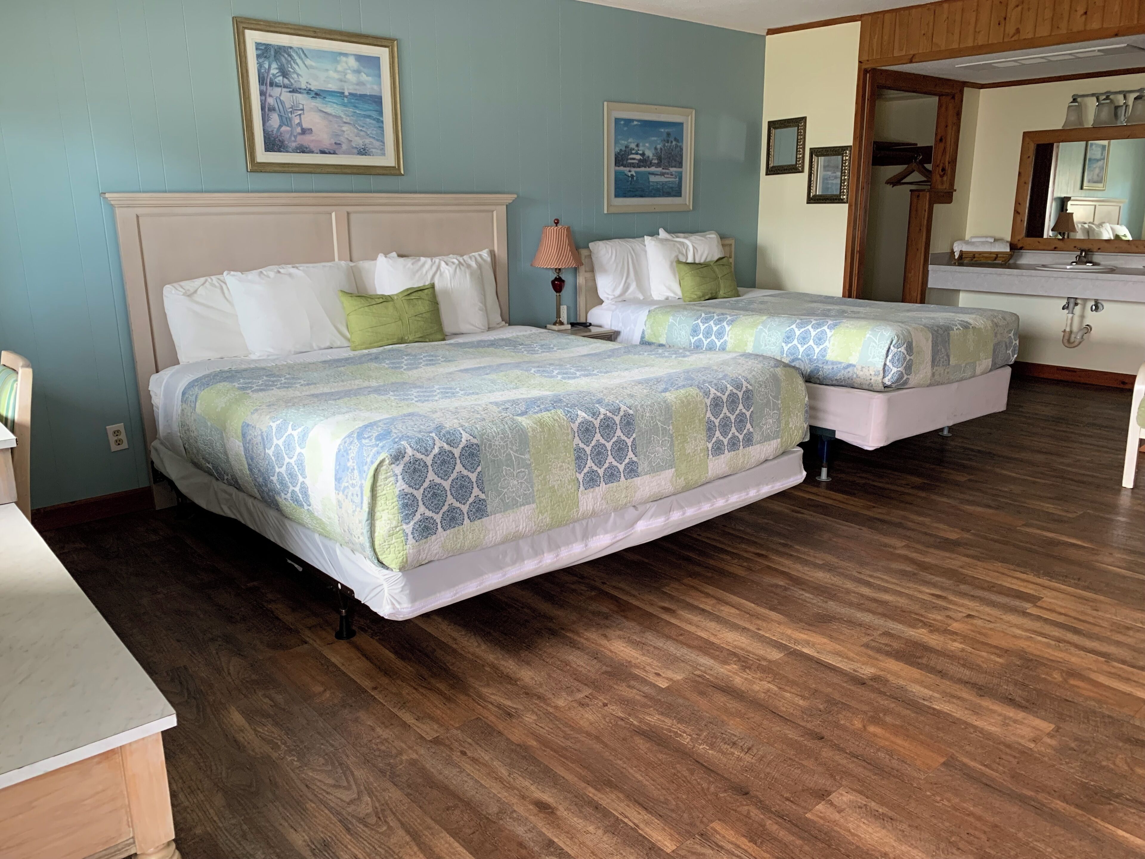 Un dormitorio con dos camas, piso de madera y baño con lavabo y espejo.