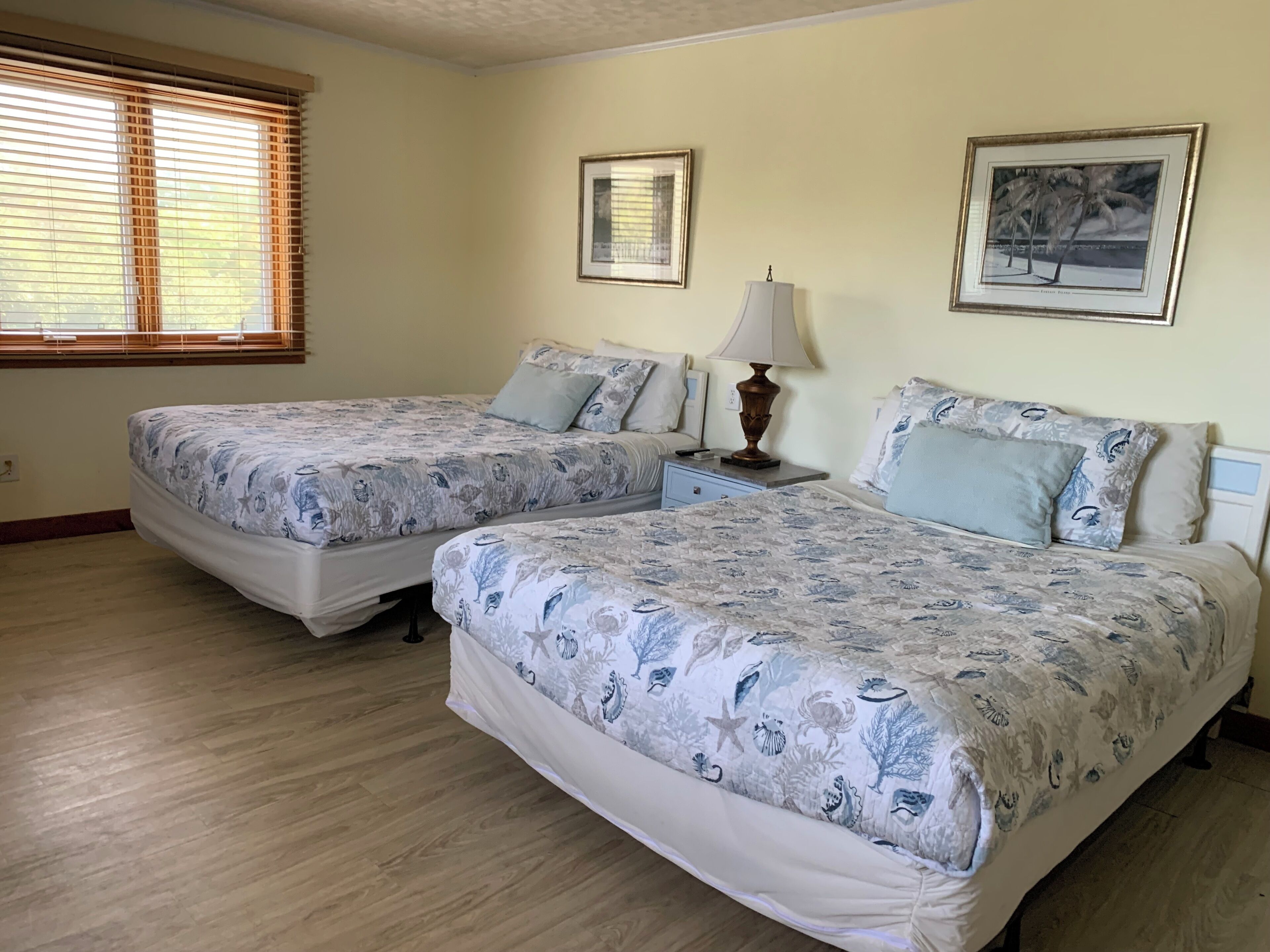 A bedroom with two beds, a nightstand, a lamp, and framed pictures on the wall.