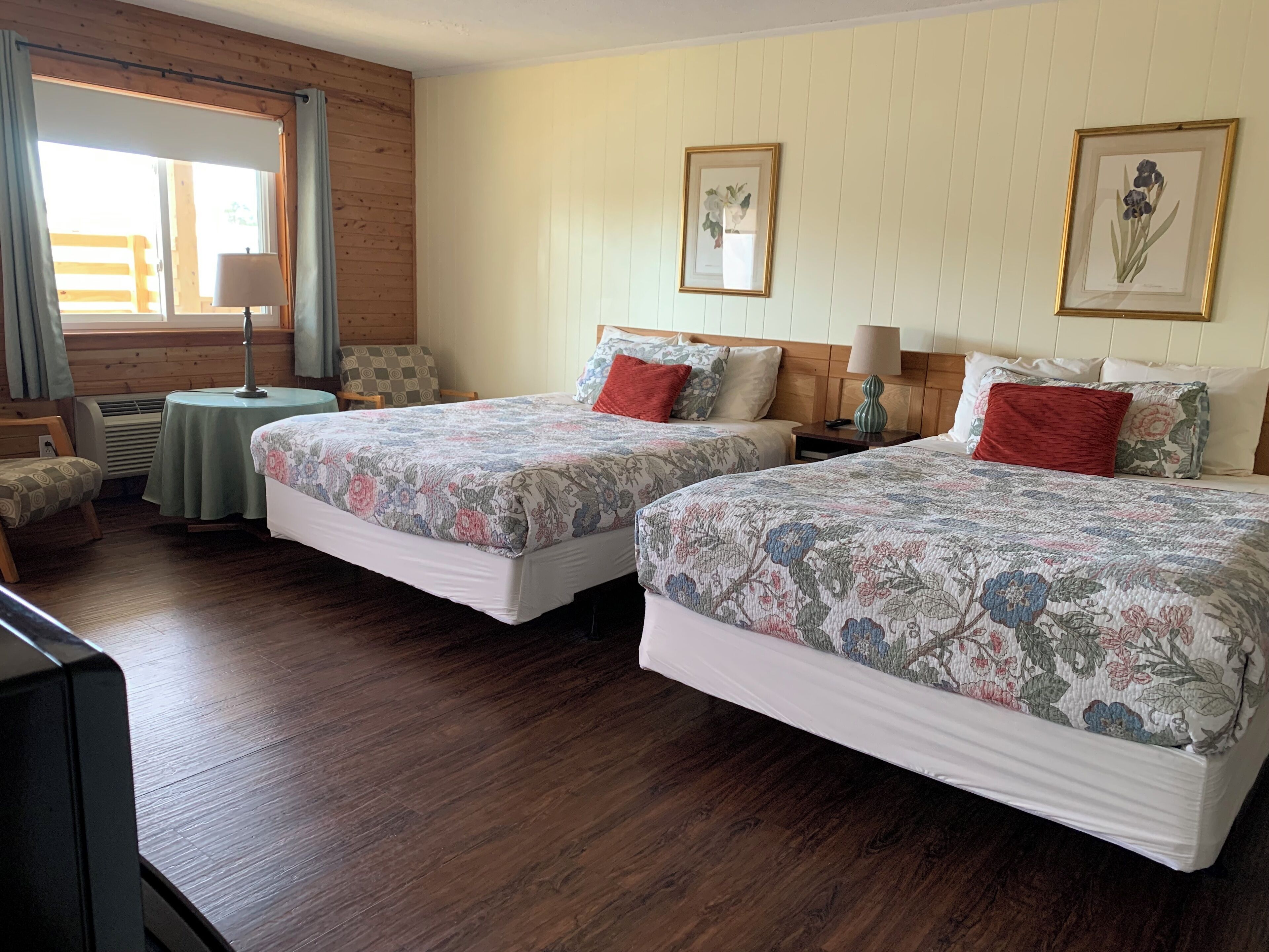 Une chambre d’hôtel avec deux lits, une petite table, une chaise et une fenêtre avec des rideaux.