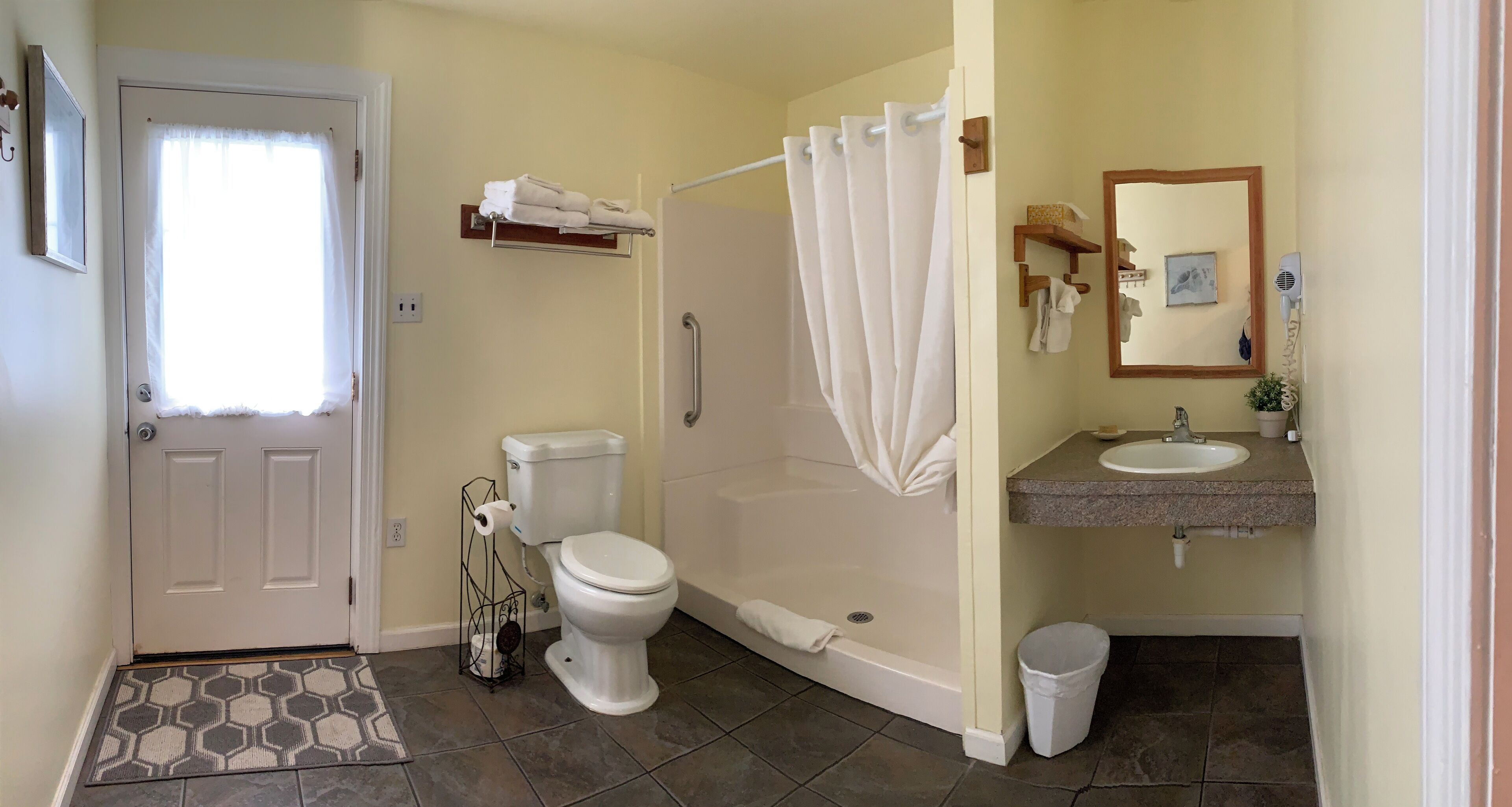 A bathroom with a toilet, shower, sink, and a small mirror.