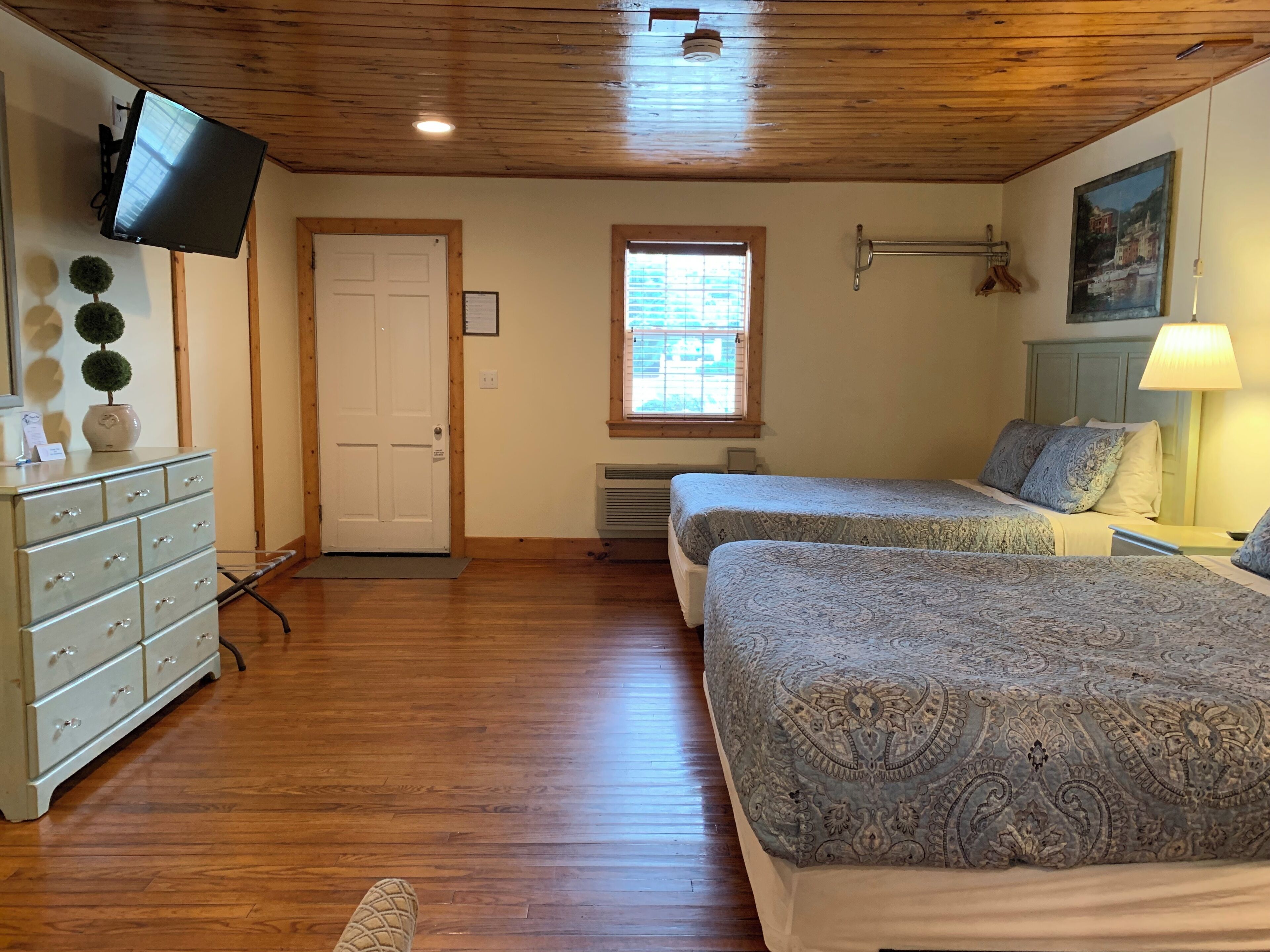 Une chambre avec deux lits, une commode, un téléviseur, une fenêtre et un tableau.
