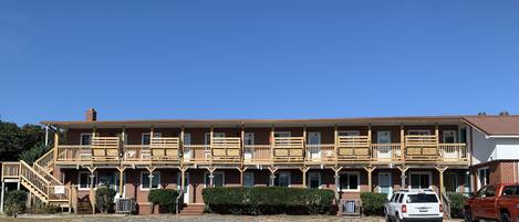 A two-story motel with wooden balconies, a central staircase, and a gravel driveway.