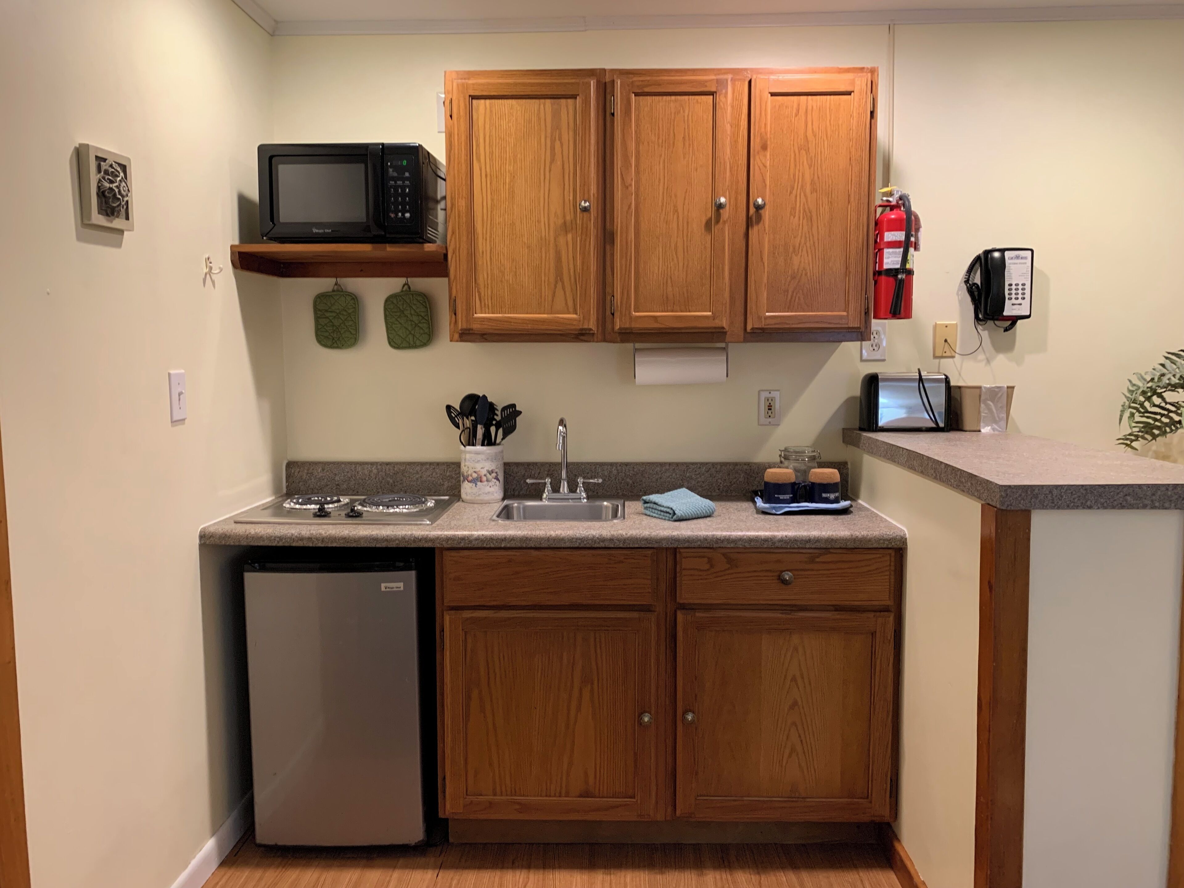 A compact kitchen with wooden cabinets, a microwave, a dishwasher, and a small countertop.