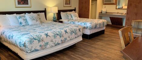 A hotel room with two beds, a wooden floor, a desk, and a bathroom visible through an open door.