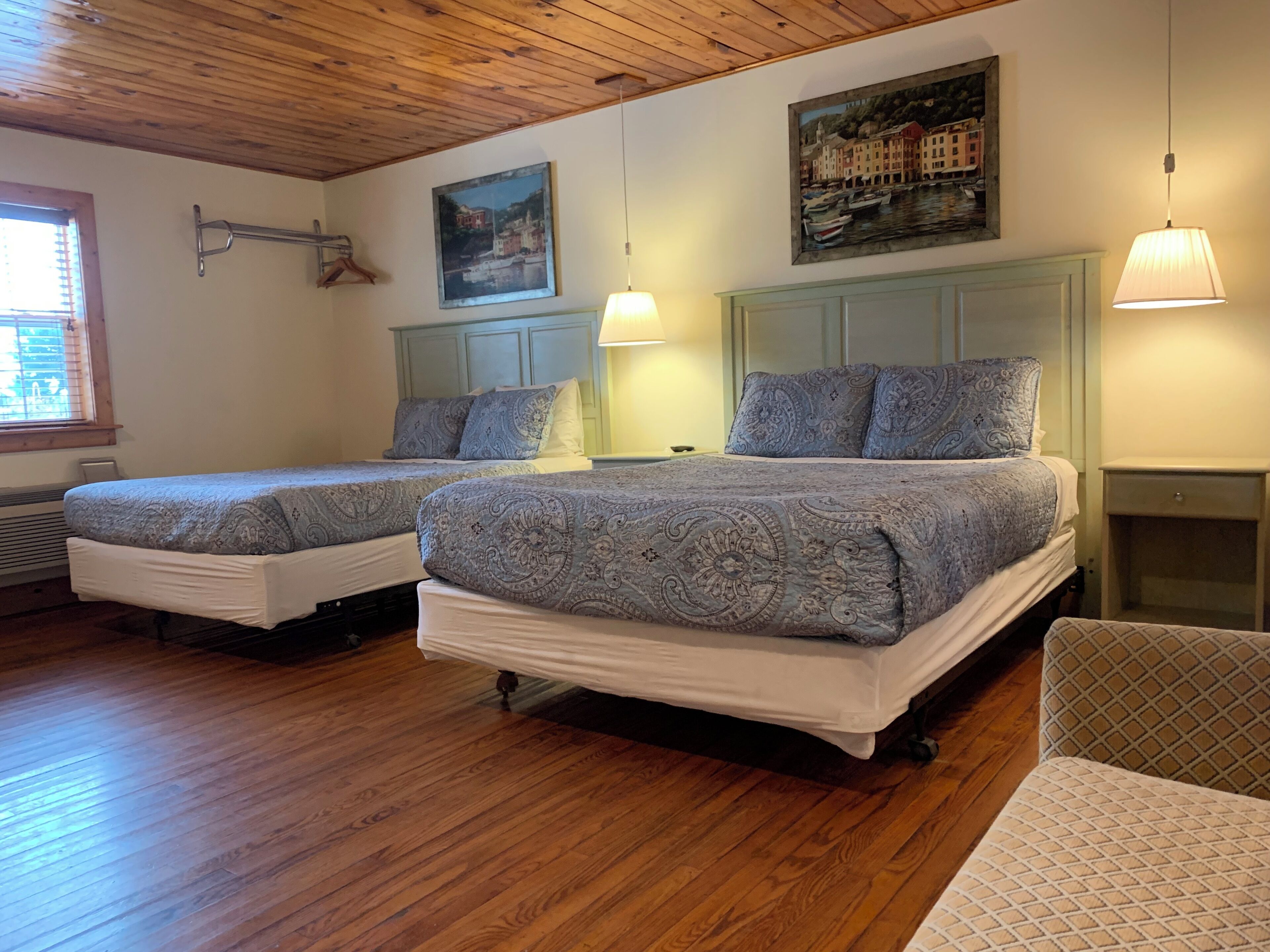 A bedroom with two beds, wooden flooring, a painting, and a lamp.