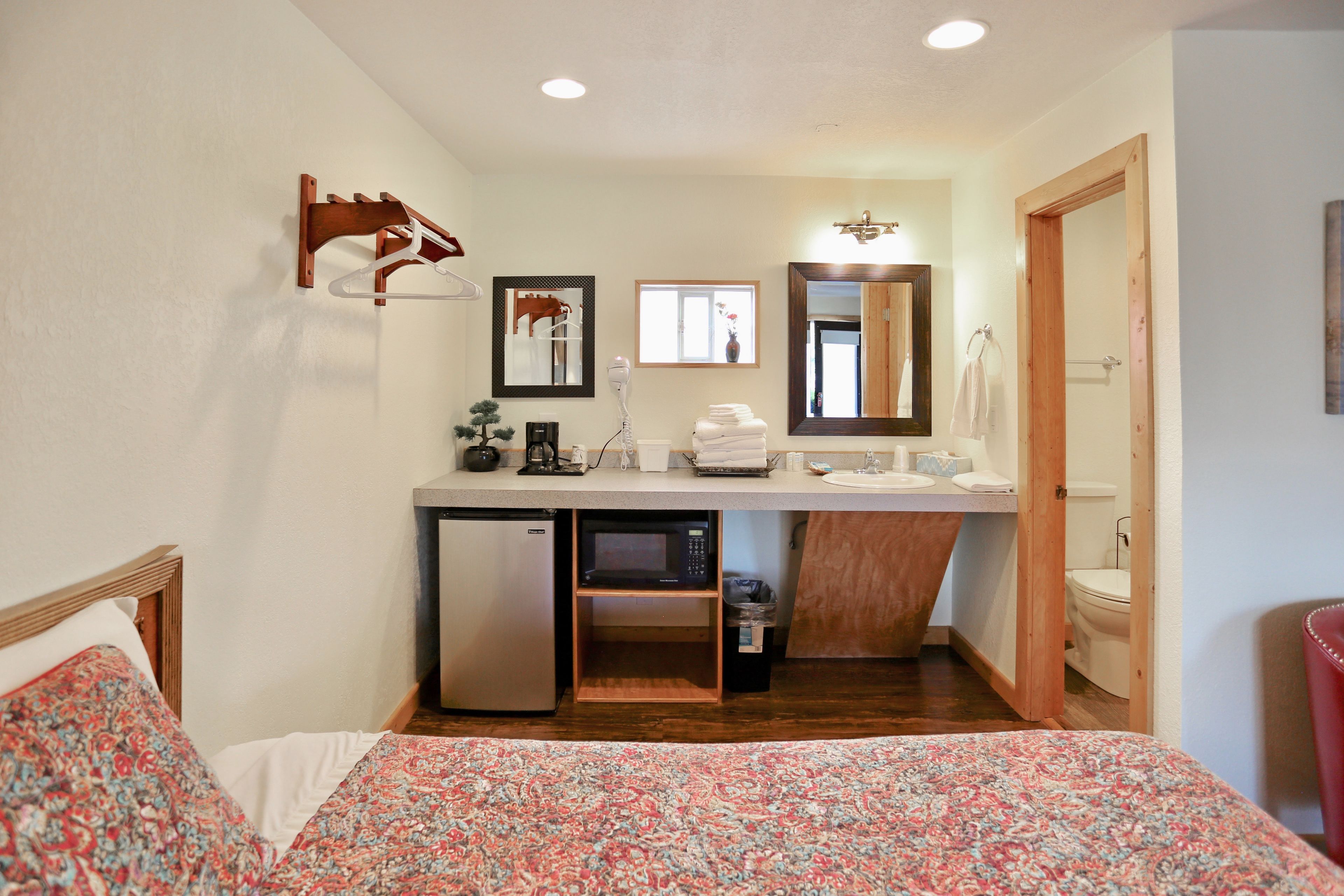 Habitación de hotel compacta con cama, kitchenette, microondas, refrigerador, lavamanos y retrete.