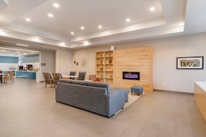 A modern living area with a sofa, a wooden entertainment unit, and a kitchen in the background. - Country Inn & Suites by Radisson, Savannah Airport, GA (Savannah)