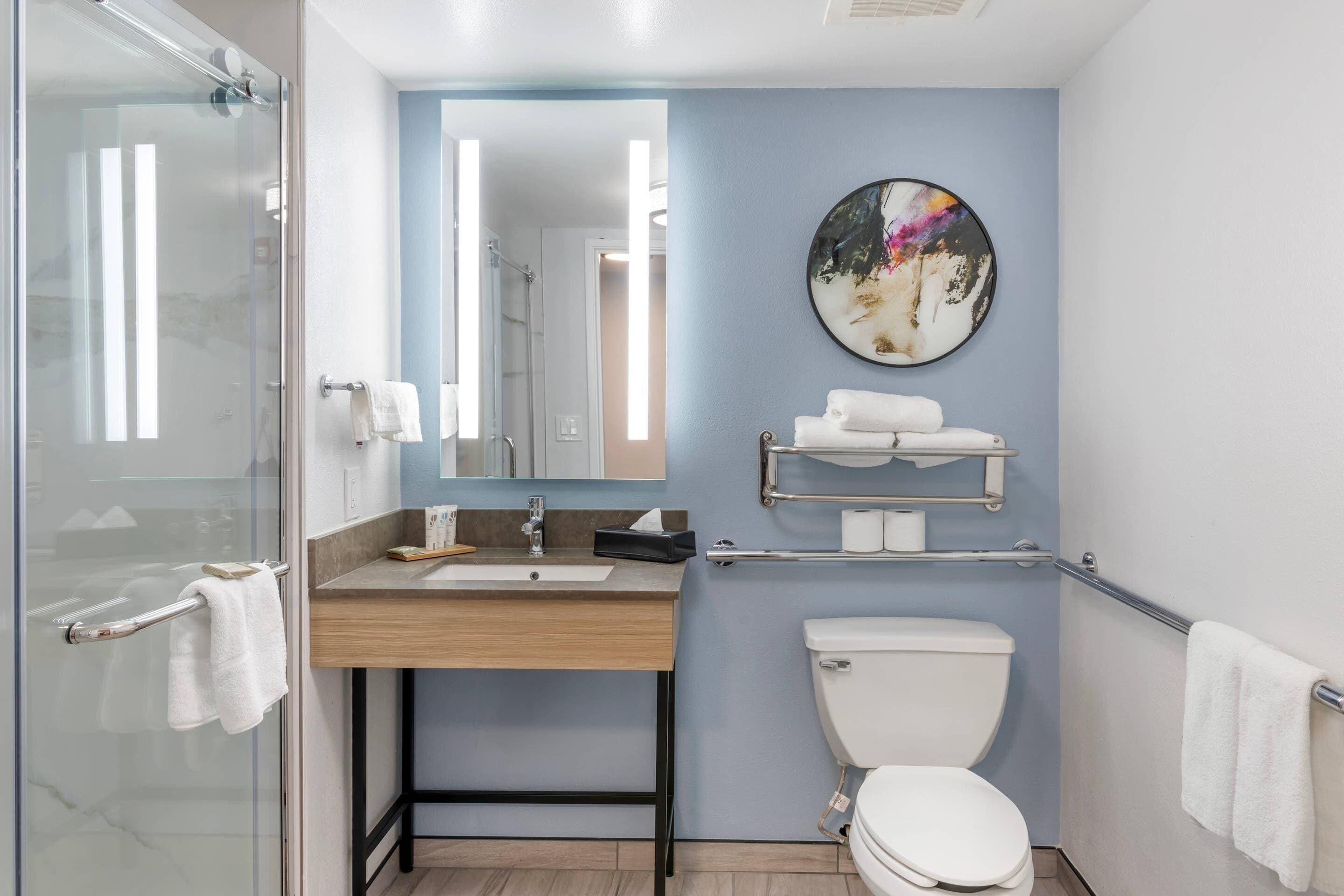 A modern bathroom with a glass shower enclosure, a wooden vanity with a sink, a toilet, and a towel rack.